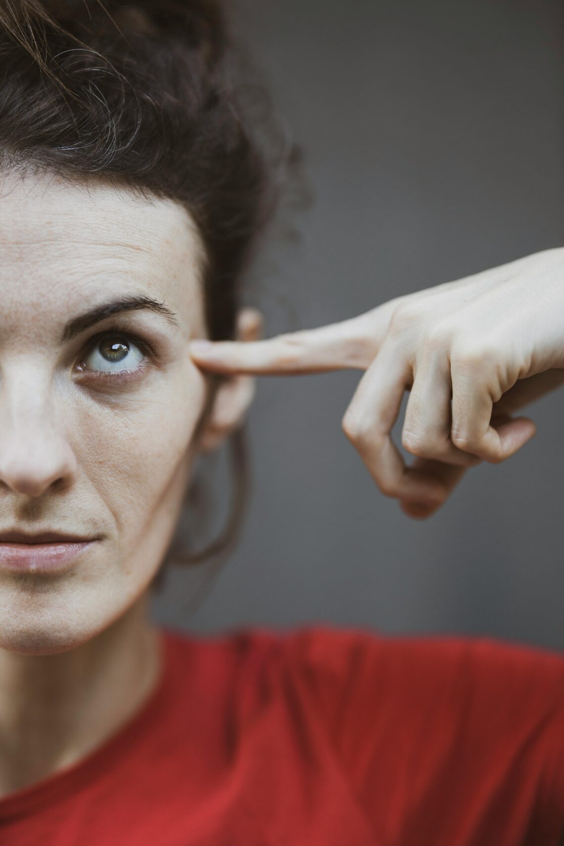 Selective focus portrait photo of woman in red t shirt pointing to her head