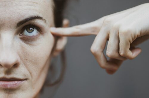 Selective focus portrait photo of woman in red t shirt pointing to her head